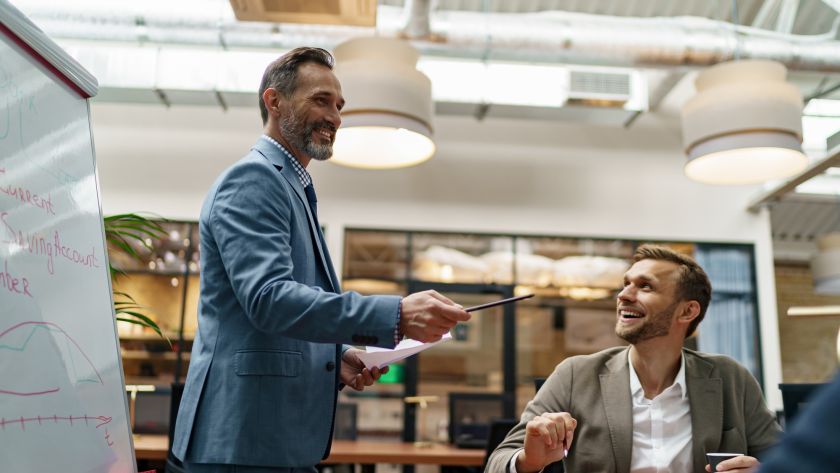 Mature business coach or speaker make flip chart presentation to diverse businesspeople at meeting